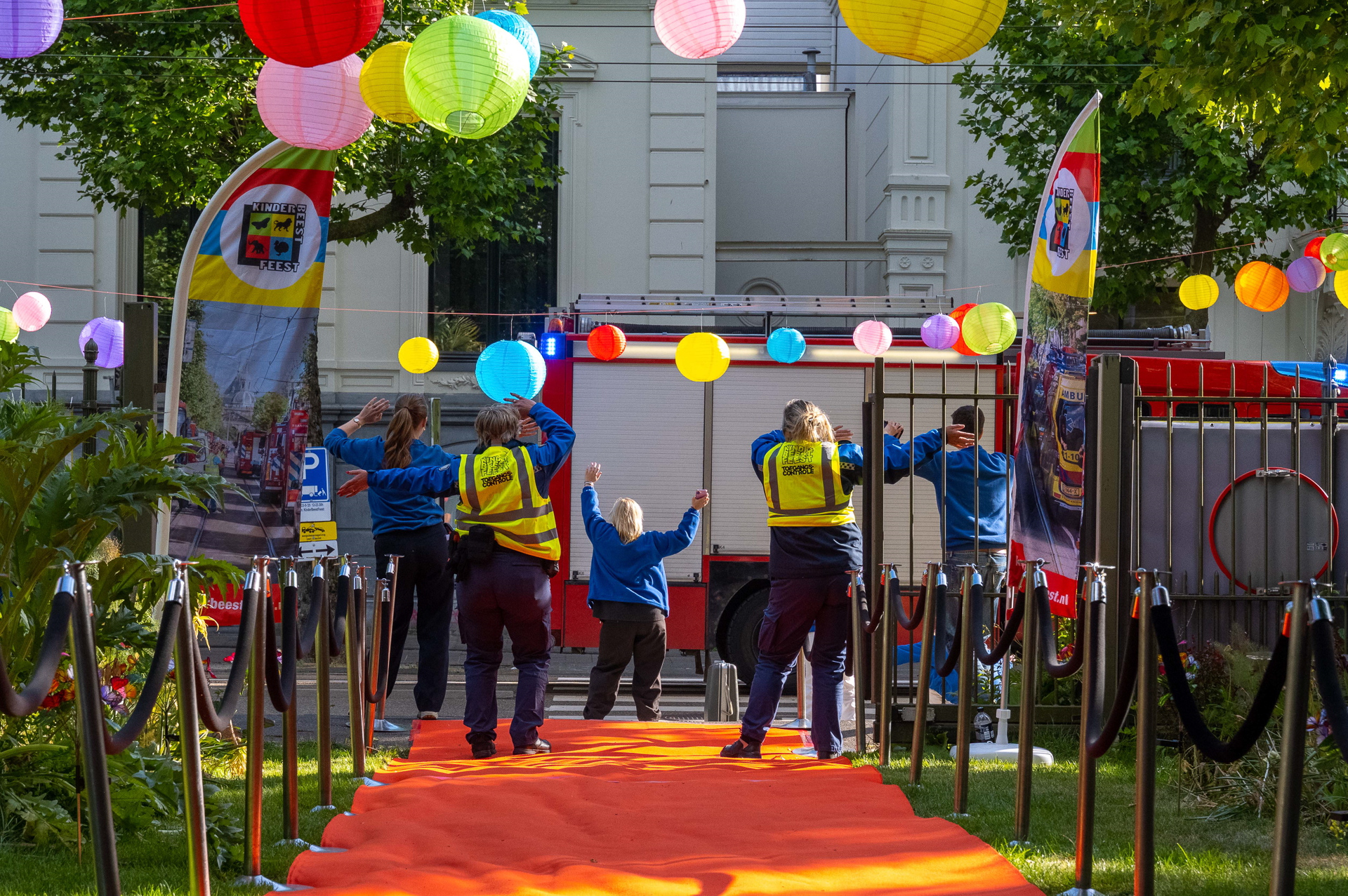 Hulpverleners juichen bij een brandweerwagen onder gekleurde lampionnen bij de entree van het KinderBeestFeest.