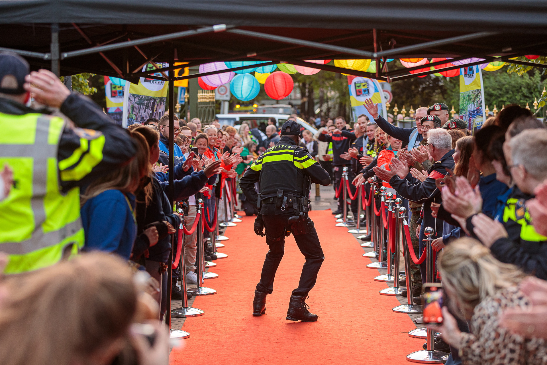 Politieagent staat dansend op rode loper terwijl vrijwilligers klappen en juichen