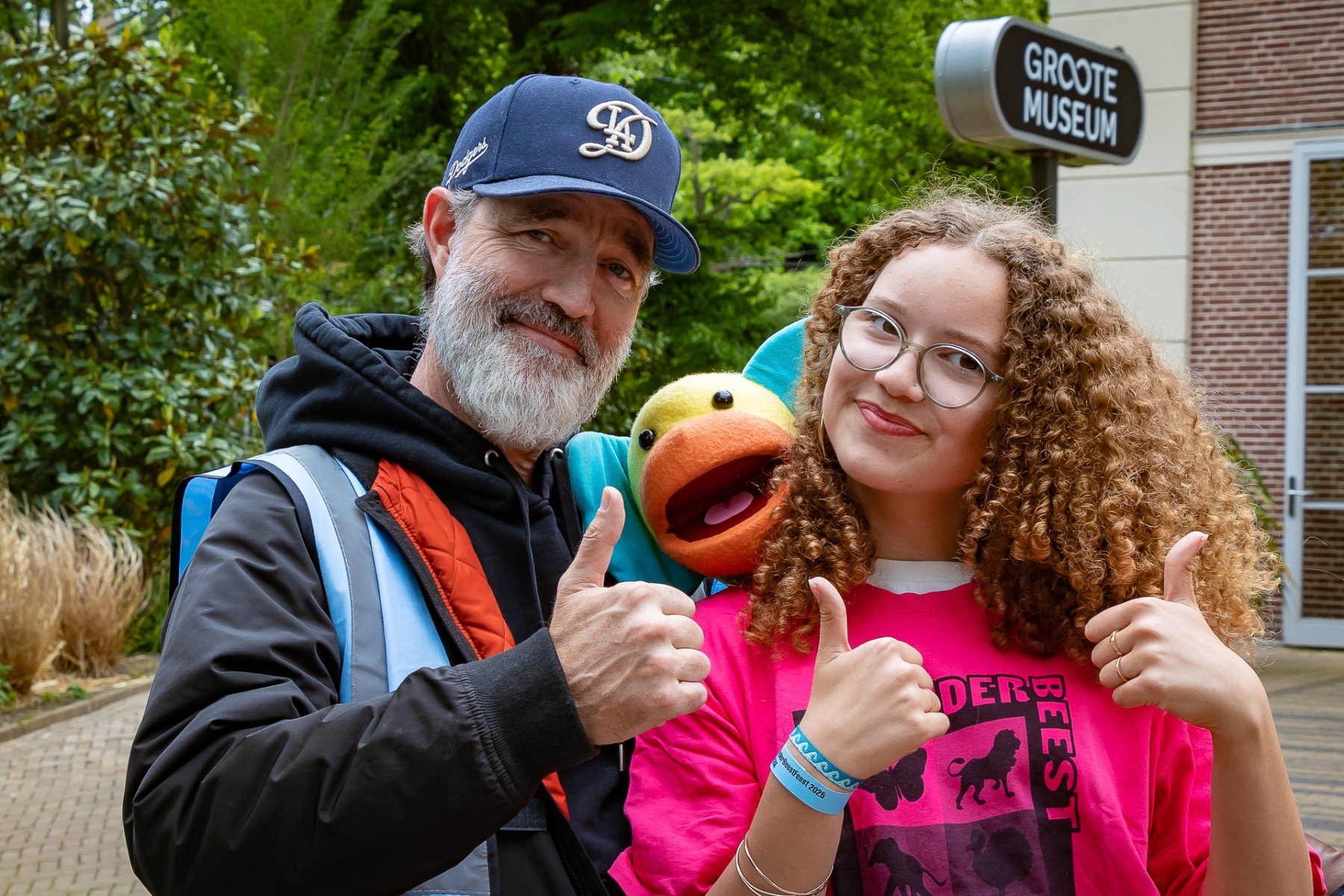 Twee vrijwilligers met een Koco knuffel in het midden steken hun duim op